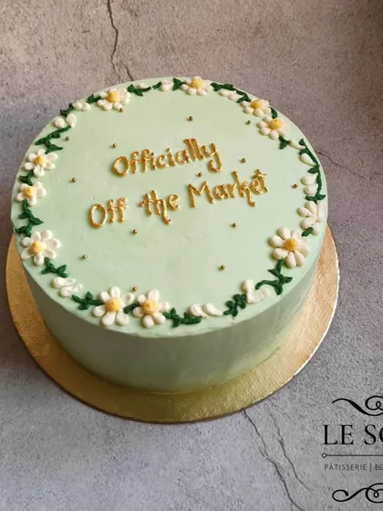 A simple and elegant design for a bridal party. This 1 kg Chocolate Caramel cake features a soft sage green buttercream, delicate hand-piped daisies, and the message "Officially Off the Market" in gold.