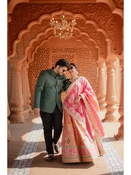 A fun and stylish pre-wedding photo of the couple walking through an ornate corridor, both wearing sunglasses and smiling.