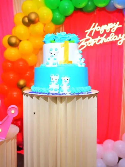 A cute two-tiered cake for a first birthday. The cake is placed on a decorative pedestal that is part of the overall party setup.