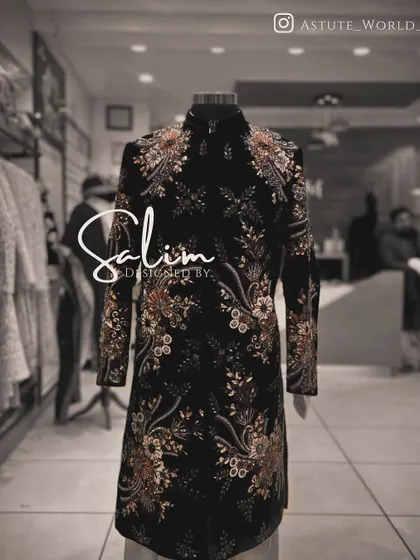 A black sherwani on a mannequin, covered in a dense floral embroidery pattern. The detail and coverage of the embroidery make it a truly luxurious piece.