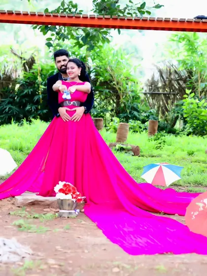 A romantic maternity photo of a couple in a park, with the woman in a vibrant pink trail gown.