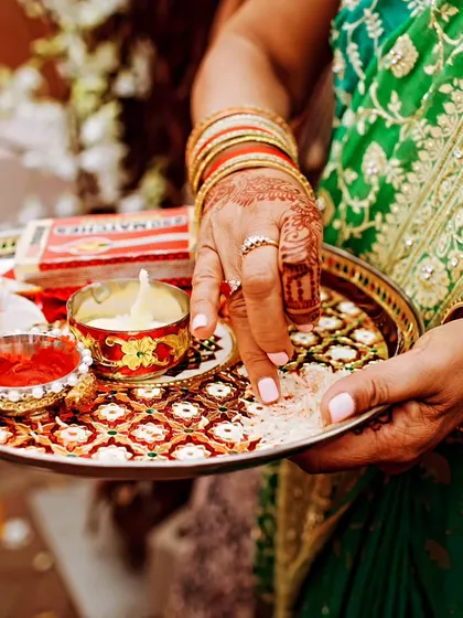 A close-up of a traditional wedding ritual, showing a hand with henna holding a decorative puja thali.