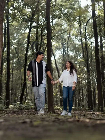 A candid shot of a couple walking hand-in-hand through a beautiful forest path. This captures a simple, happy moment in a serene natural environment.