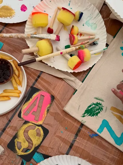 The messy, creative setup for a kids' tote bag painting party. We use stencils and sponges to make it easy and fun for little hands.