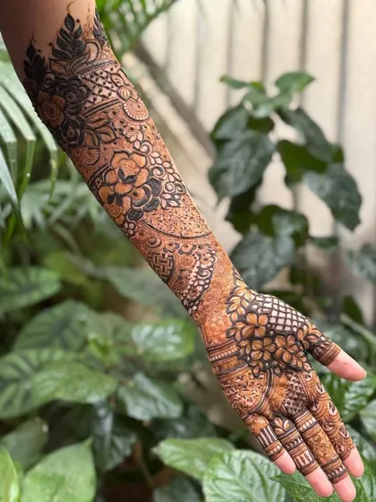 A beautiful back-of-hand design extending up the arm, set against a natural green background. The dark and light shading creates a wonderful 3D effect.