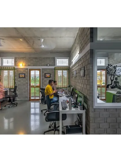 The workspace at the ASA Office, with desks arranged in an open-plan layout to foster collaboration. The fly-ash brick walls and large windows create a bright and healthy indoor environment.