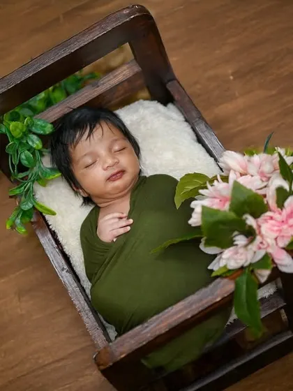 A simple, classic pose of a newborn wrapped in olive green, resting in a wooden crate. The focus is all on the baby's peaceful state.