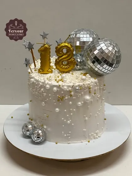 An 18th birthday cake with a fun disco theme. The white whipped cream cake is decorated with silver disco balls, stars, and pearl sprinkles, creating a festive and celebratory vibe for a milestone birthday.