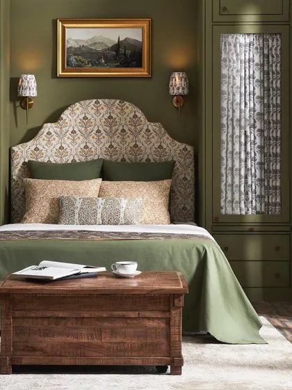 A classic bedroom setting with deep green paneled walls and traditional patterned fabrics. The styling with a rustic trunk and soft lighting creates a cozy, timeless feel perfect for heritage collections.