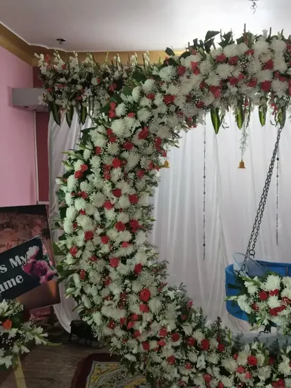 A stunning floral cradle decoration for a naming ceremony. The crescent-shaped arch is covered in fresh white and red flowers, creating a breathtaking centerpiece for the event.