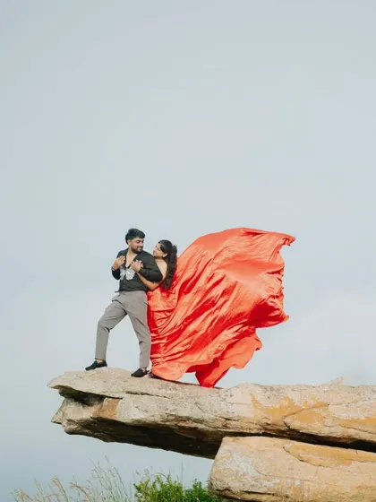 The wind catches the red trail of her gown, creating a stunning "flying" effect on the clifftop.