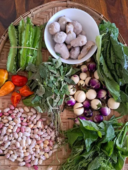 A beautiful arrangement of fresh Naga ingredients on a woven bamboo tray. This includes Raja Mircha, bitter eggplant, kidney beans, taro, and various wild greens, all essential to our cuisine.