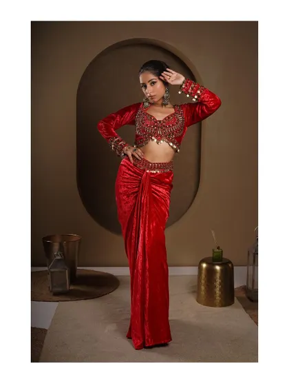 A powerful full-length shot of a modern red velvet saree. The studio lighting brings out the rich texture of the velvet and the intricate details of the embellished blouse.