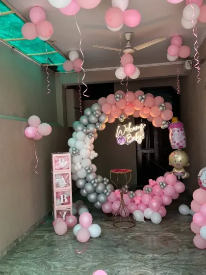A beautiful "Welcome Baby" setup for a baby girl in a pink, white, and silver chrome color scheme. It features a circular balloon garland, a neon sign, and 'BABY' display boxes, all arranged to create a memorable welcome.