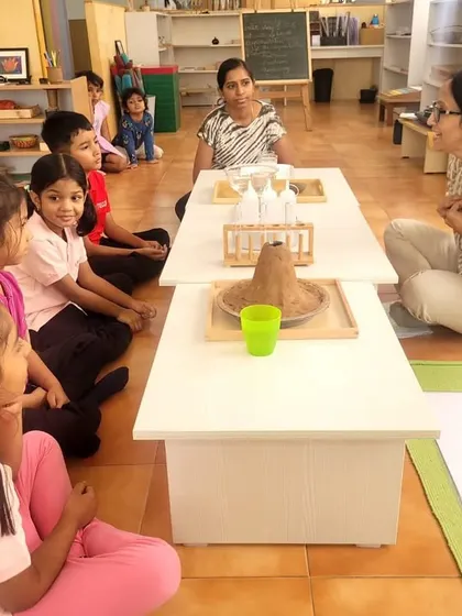 A teacher engages the children with the story of the universe, using a model volcano to illustrate Earth's formation. Storytelling makes complex scientific ideas accessible and exciting.