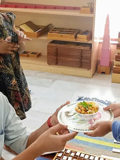 A child proudly serves the finished chickpea salad to a teacher. Learning to serve others is an important Montessori grace and courtesy lesson that we practice daily.