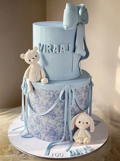 A lovely two-tiered blue cake with a toile pattern, perfect for a baby boy's 100-day celebration.