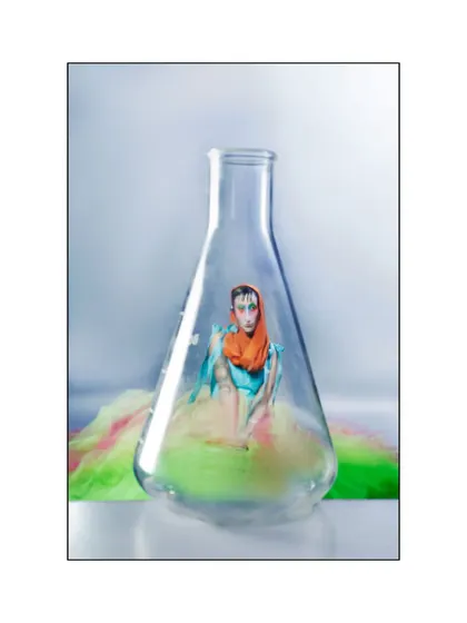 A surreal composition where the model, in her colorful gown, is captured inside a large laboratory flask. This image literally frames the concept of human emotion as a contained, observable chemical experiment.