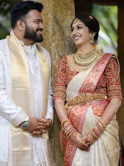 A happy couple poses between the stone pillars of the mantapa, a timeless setting for a classic wedding portrait.