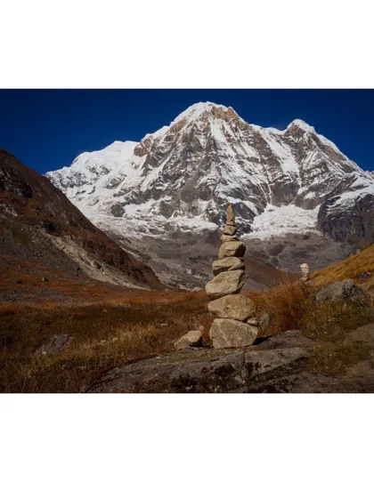 A moment of peace and balance. A trekker's cairn stands against the backdrop of the mighty Annapurna massif, a symbol of respect and mindfulness in the high mountains.