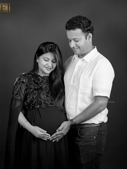 A classic black and white couple's portrait. The focus is entirely on their expressions and the gentle way they hold the baby bump together.