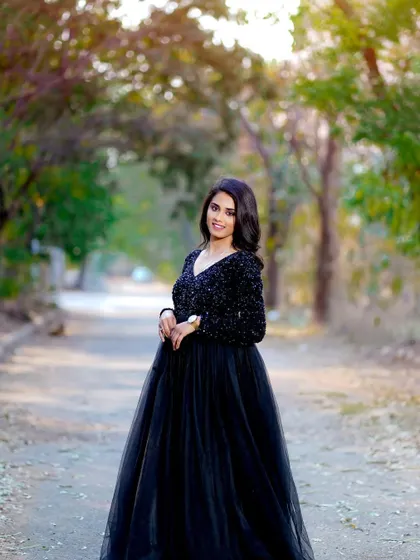 A confident stance during an outdoor fashion shoot. The makeup is glamorous and polished, perfect for the elegant black gown and natural setting.