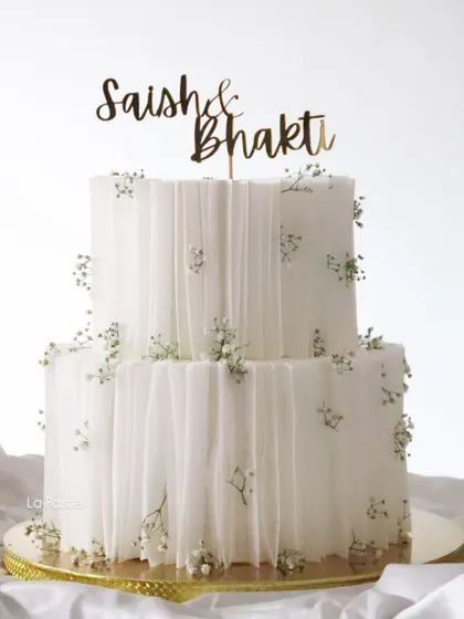 So simple, yet so stunning. This two-tier engagement cake is wrapped in delicate, edible wafer paper to create a fabric-like effect, dotted with tiny baby's breath flowers and finished with a custom name topper.