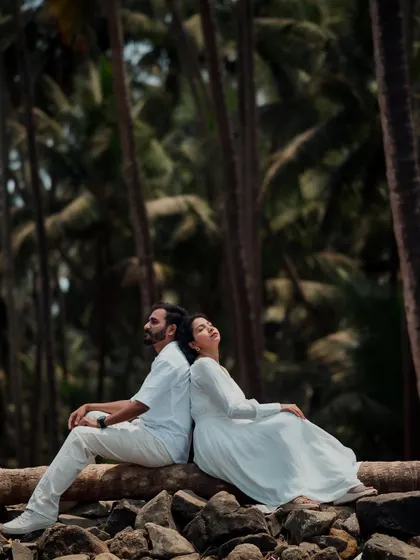 A serene and artistic shot of a couple resting back-to-back on a log. The towering palm trees in the background create a beautiful, natural frame for this peaceful pre-wedding moment.
