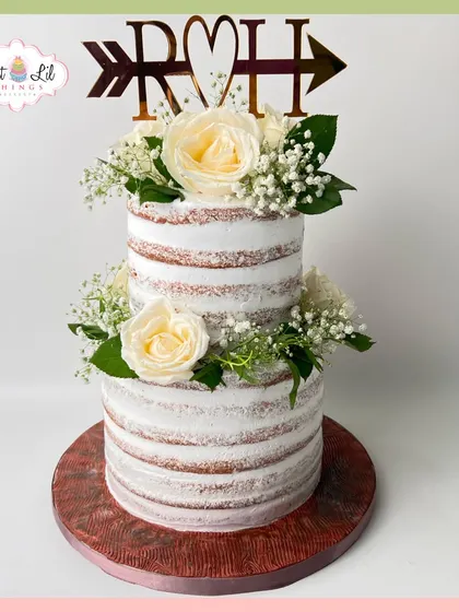 A beautiful two-tiered rustic wedding cake. The "naked" style is adorned with fresh white roses and baby's breath for a simple, elegant look.