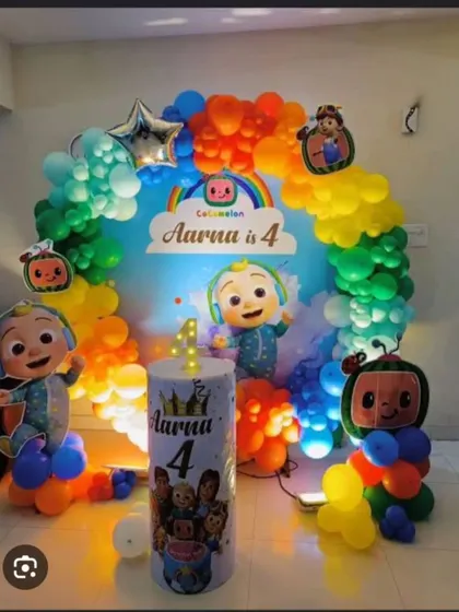 A Cocomelon theme for Aarna's 4th birthday, featuring a circular balloon arch in rainbow colors, character cutouts, and a personalized pedestal for the cake.