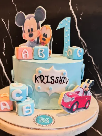 A classic Mickey Mouse themed cake for a first birthday. The design features Mickey and Pluto, along with personalized letter blocks, making it a perfect choice for a little one's special day.