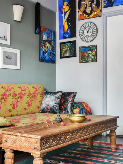 This corner is a celebration of color and personal art. A floral sofa, a carved wooden coffee table, and a gallery wall of the owner's paintings create a vibrant, bohemian feel.