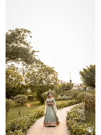 A wide shot that sets the scene, showing the model in a beautiful green lehenga walking through a lush garden path. This environmental portrait tells a larger story and highlights the grandeur of the setting.