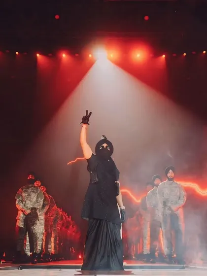 Diljit Dosanjh making a powerful statement on stage. The dramatic spotlight and the formation of his backup performers create a scene of strength and unity.