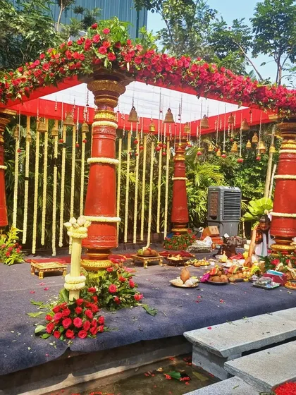 A grand South Indian mandap with red pillars, set up outdoors for a beautiful daytime wedding.