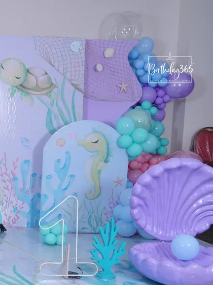 A close-up of the decor for a first birthday under the sea, featuring a large "1" sign, a giant clamshell, and a seahorse-themed backdrop.