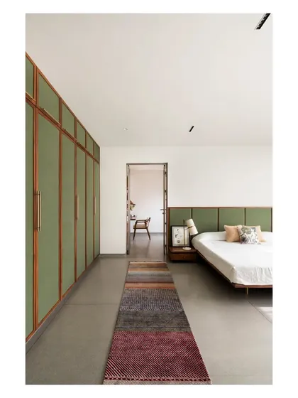 The master bedroom, with its serene moss-green headboard and wardrobes set against a cool grey terrazzo floor. The long runner rug adds a splash of color and texture.
