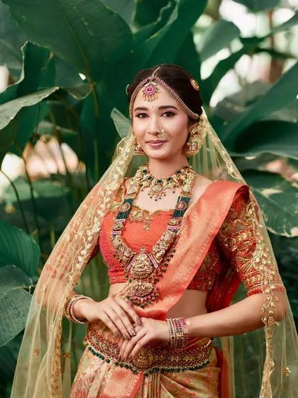 A signature muhurtham look created for a professional bridal course. This style features a layered temple jewellery set with green and pink stones, a matha patti, and a delicate nose ring, perfect for a classic South Indian bride.