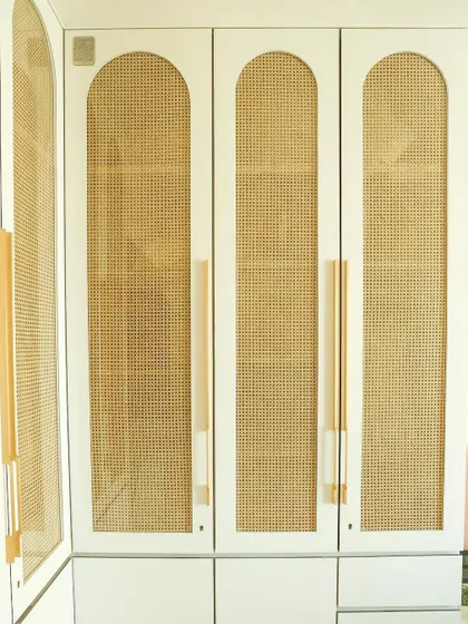 A close-up of the wardrobe's arched rattan panel and elegant long brass handle, a detail that elevates the entire piece.