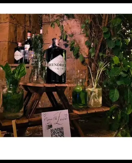 A rustic gin bar setup nestled amongst natural greenery. This 'garden bar' concept uses wooden stands and glass jars filled with fresh herbs and botanicals for a truly organic feel.
