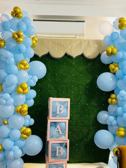 A simple yet elegant baby shower decoration with two balloon pillars in blue and gold, and transparent "BABY" blocks in the center.