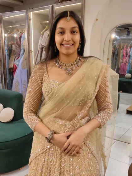 A happy client trying on a golden sequined lehenga. She paired it with a simple, elegant antique-finish necklace for a sophisticated wedding guest look.