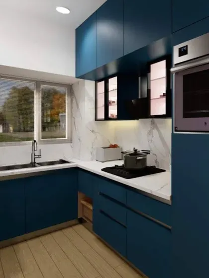 A stunning modular kitchen in a deep blue matte finish. The design includes a white marble-effect backsplash, integrated oven, and clever use of corner space, combining bold color with smart functionality.