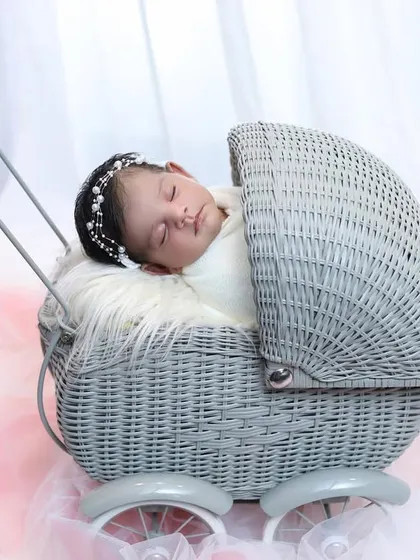 A full view of the baby sleeping in the classic grey wicker pram against a soft pink backdrop. This prop is versatile and perfect for timeless baby portraits.