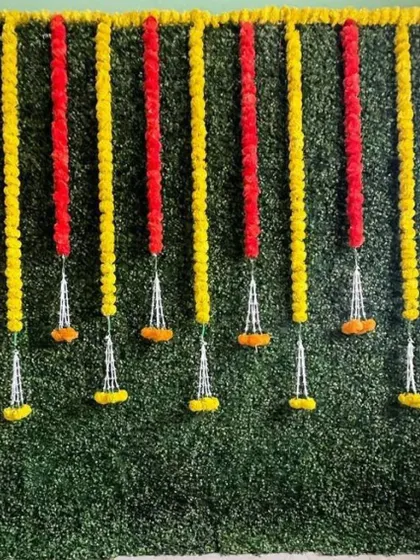A greenery wall decorated with red and yellow marigold garlands. This classic color combination is perfect for traditional Indian ceremonies and celebrations.