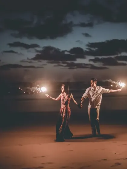 A wide shot of the couple with sparklers on the beach at night, creating a beautiful and dramatic image.