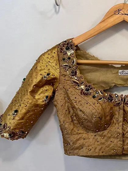 A classic gold Kanjeevaram bridal blouse, elevated with hints of green beads and intricate floral embroidery around the neckline and back cutout.