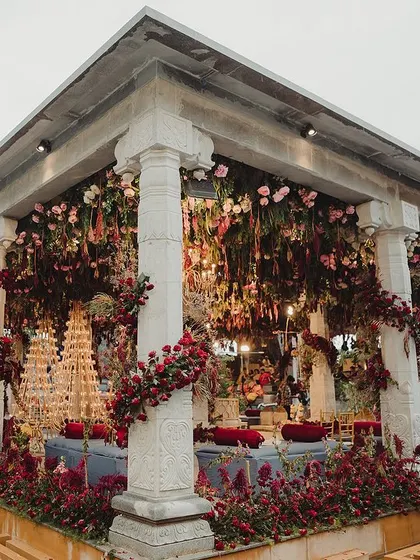 A wide view of the stunning Bunt ceremony we designed by the hills. The structure is adorned with layers of flowers in deep, rich colors, creating a dramatic and opulent setting against the natural landscape.