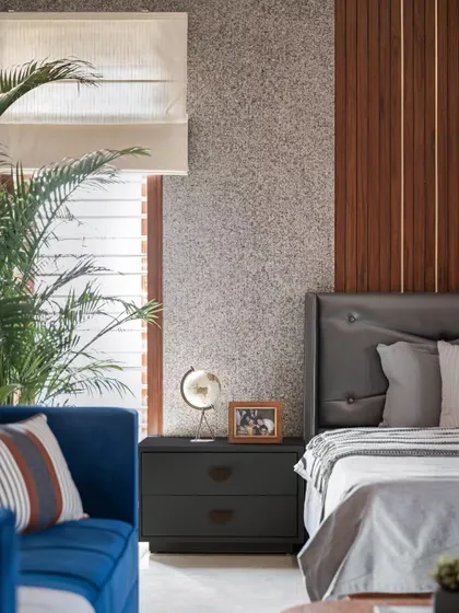 A detail shot of the bedroom with the textured stone-finish wall. The combination of the rough wall, the smooth wood paneling, and the soft fabrics on the bed creates a tactile and visually interesting space. The blue sofa adds a strong color accent.