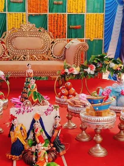 A complete platter decoration for a half-saree ceremony. The setup includes dolls, decorated fruit baskets, and sweet trays, all arranged to create a festive and colorful display.